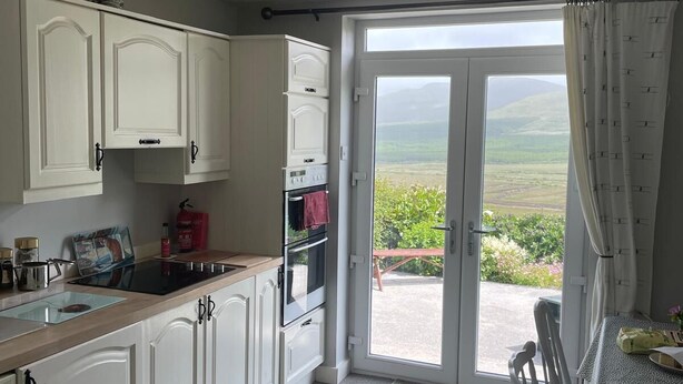 A kitchen with white cabinets, a stove, and a dining area with a table and chairs. - Jerry's Cottage, Dingle Penninsula Wild Atlantic Way and Páirc Nasiúnta na Mara  (Co)