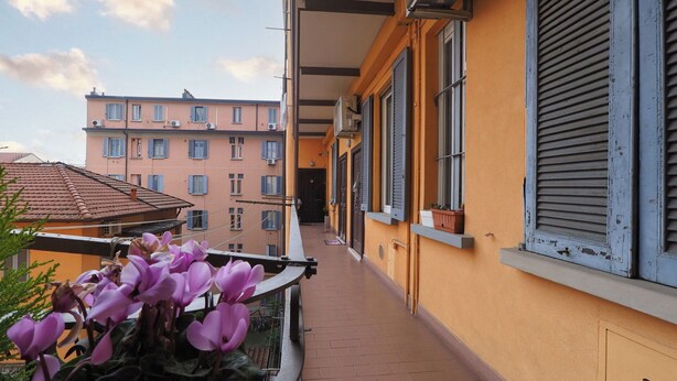 Un balcone stretto con vista su un edificio rosa e un cielo sereno.