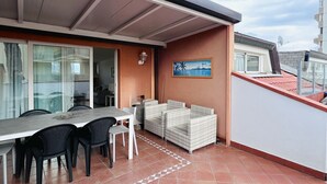 A balcony with a dining table and chairs, a sofa, and a painting. - Attic Gardens Flexrent - Abyssinia (Riccione)