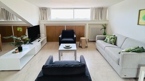 A modern living room with a sofa, armchair, and a TV on a white console. - Attic Gardens Flexrent - Abyssinia (Riccione)