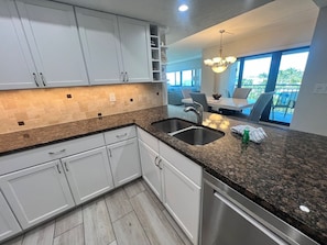 A modern kitchen with white cabinets, granite countertops, and a stainless steel dishwasher. - Best view on Siesta Key | Walk Right onto Siesta Key Beach (Sarasota)