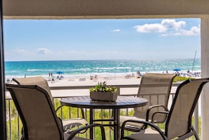 A balcony with a table and chairs, overlooking a beach with people and umbrellas. - Relax and unwind at Villa 212 in Siesta Sands (Sarasota)