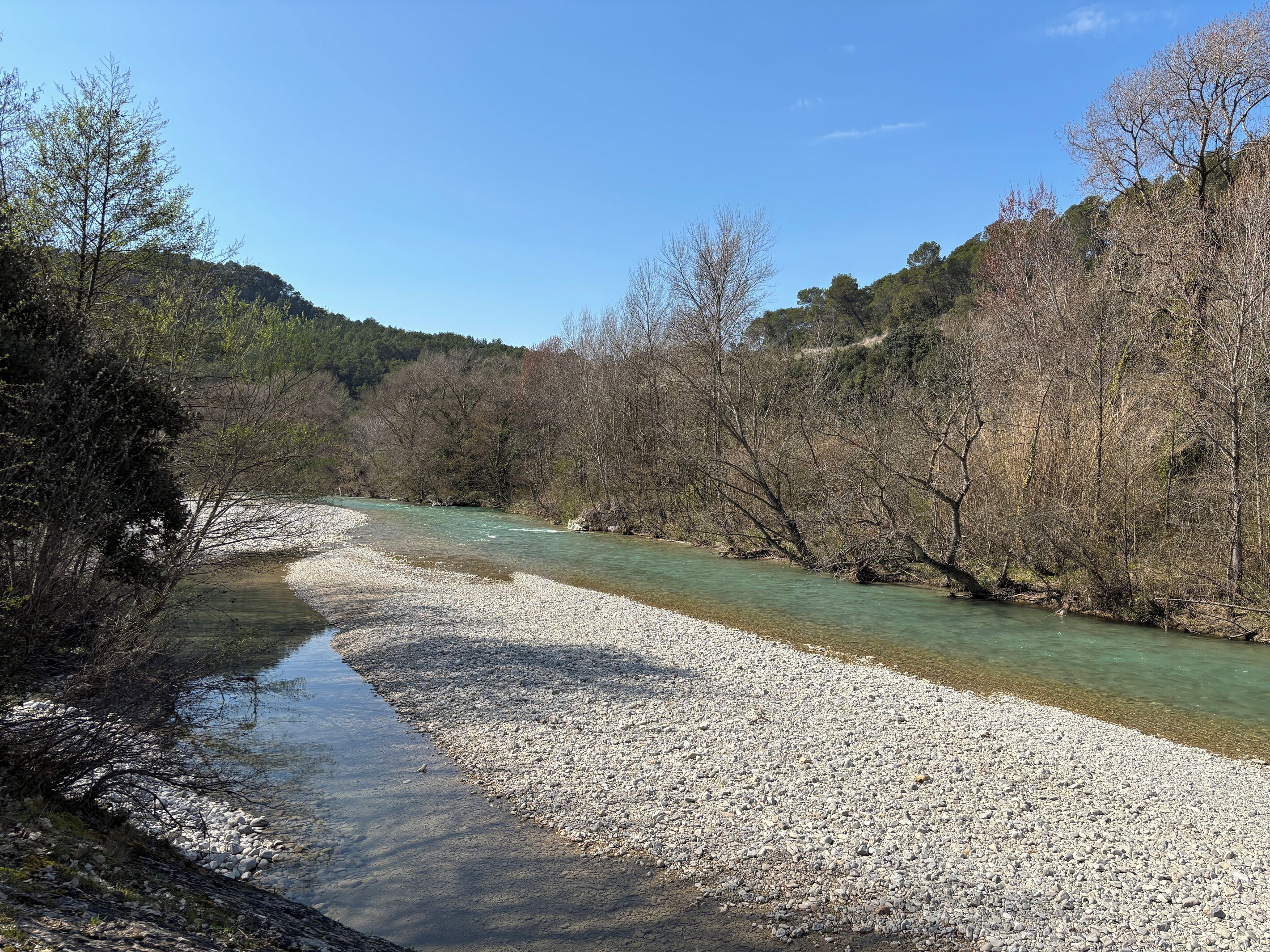 Um rio com águas cristalinas, rodeado por árvores e uma margem rochosa.