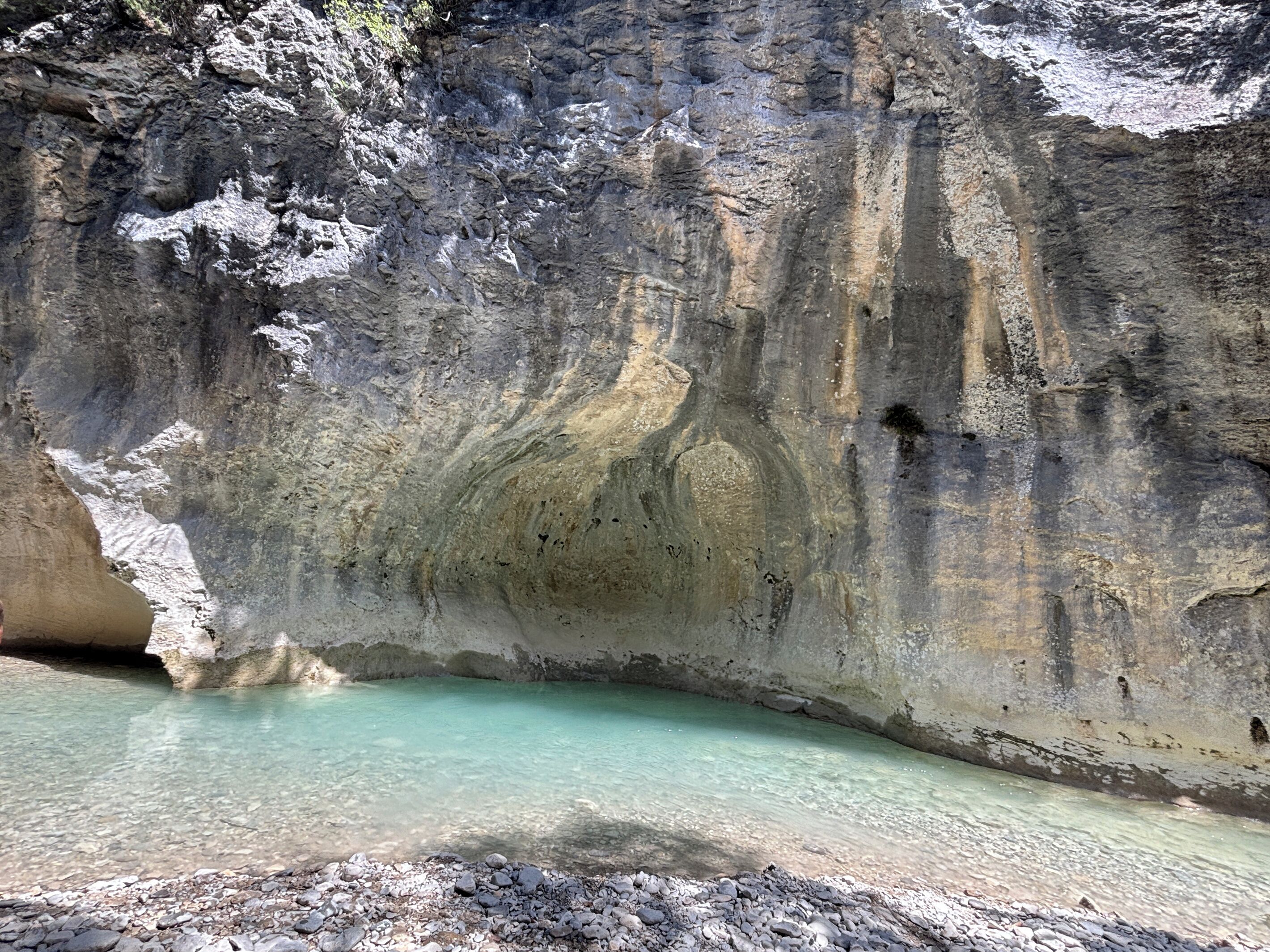 A natural rock formation with a clear water pool at its base.