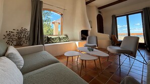 Ein Wohnzimmer mit einer Couch, zwei Sesseln, einem kleinen Tisch und einem Fenster mit Blick auf Bäume und ein Gebäude.