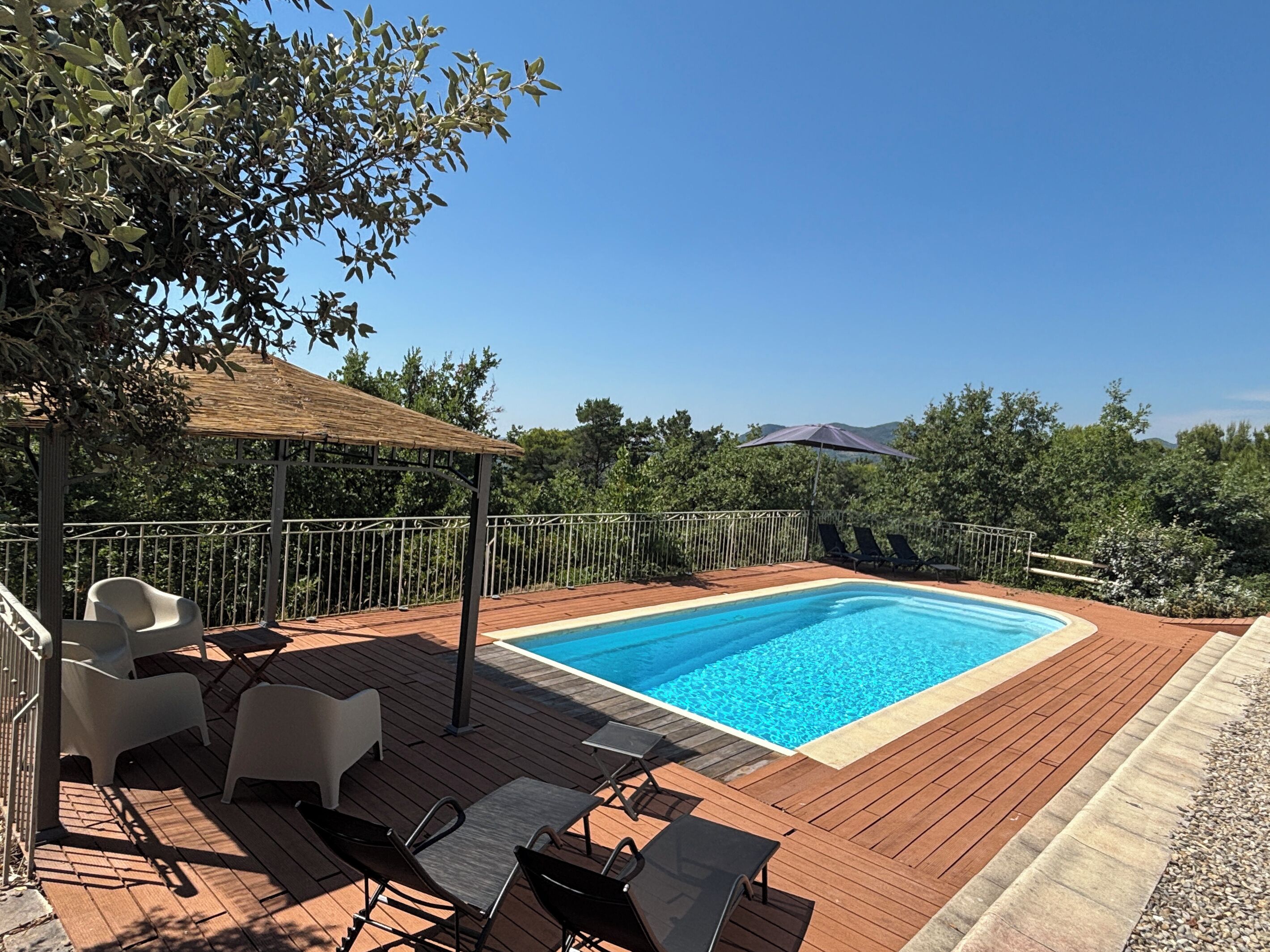 A swimming pool with a wooden deck, lounge chairs, and a pergola.