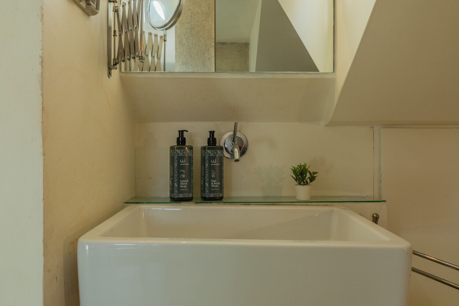 A bathroom with a white bathtub, a glass shelf holding two bottles of liquid soap, and a small potted plant.
