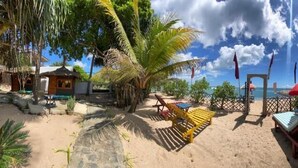 A beach area with a pathway leading to a gate, surrounded by palm trees and beach chairs.