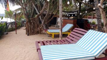Ein Strandbereich mit zwei gestreiften Liegestühlen, einer Holzkonstruktion und Lichterketten.