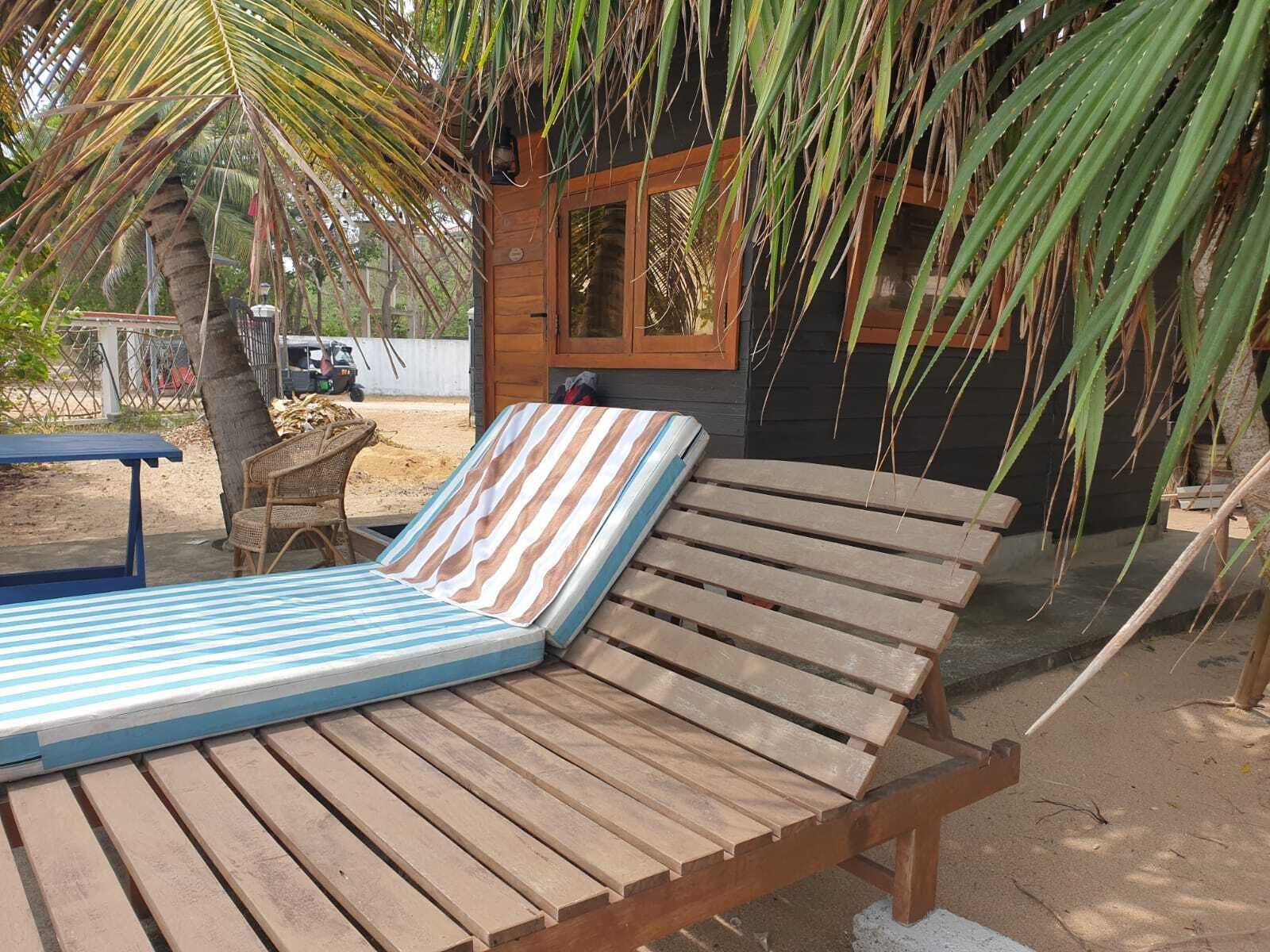 A wooden lounge chair with a striped cushion, a small wooden table, and a palm tree in the background.
