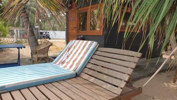 A wooden lounge chair with a striped cushion, a small wooden table, and a palm tree in the background.
