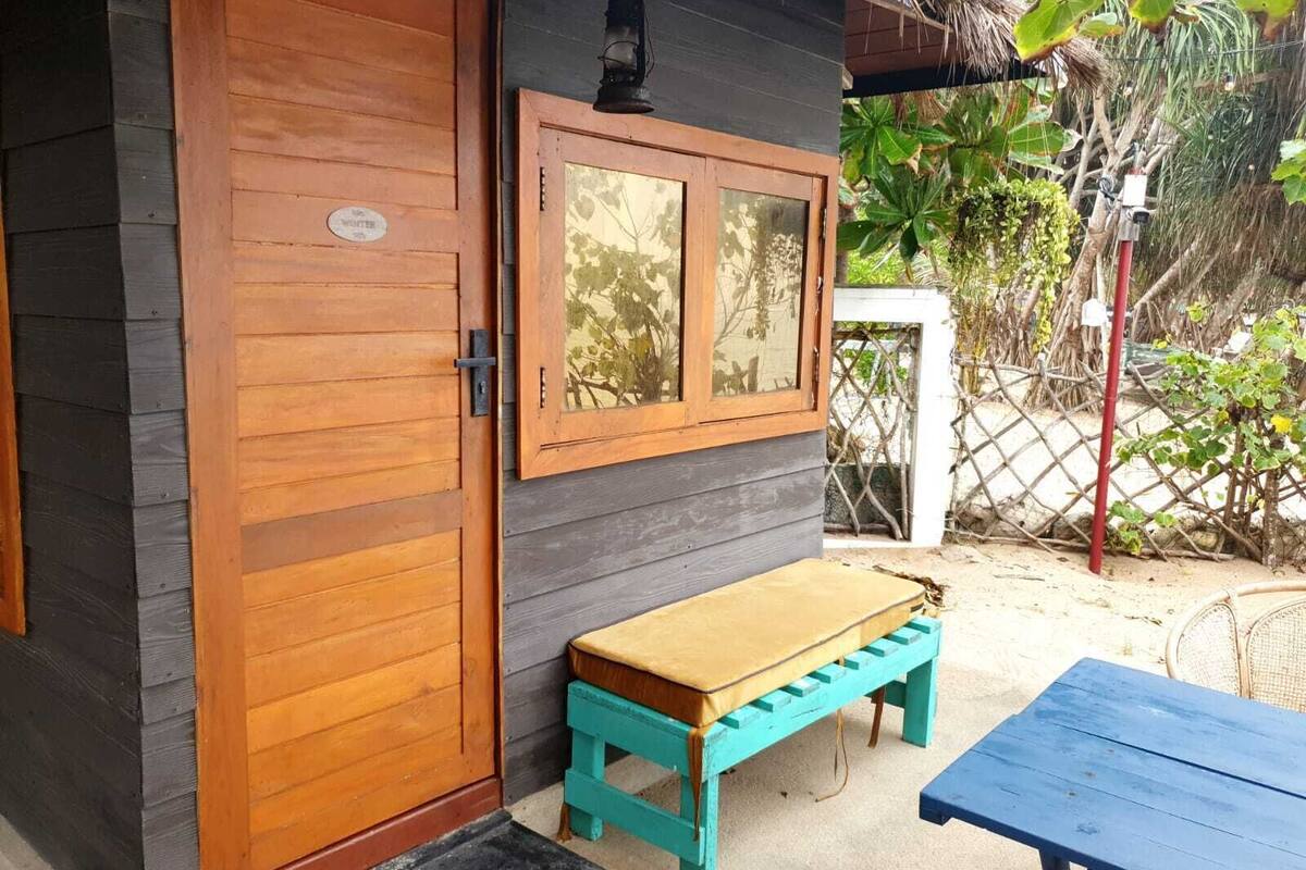 A wooden door with a small window, a bench, and a table outside a building.