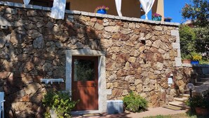 A stone building with a wooden door, a small step leading to the entrance, and potted plants around the area. - IL GIARDINO DI DANIELA APARTMENTS (San Teodoro)