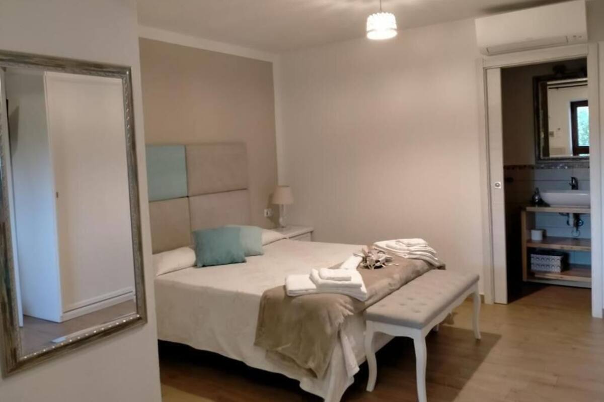 A bedroom with a bed, bedside table, bench, and a mirror.