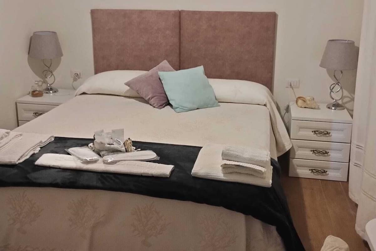 A neatly made bed with a pink headboard, two bedside tables with lamps, and a bedside table with a decorative item.