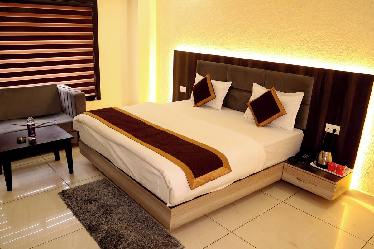 A hotel room with a bed, a sofa, a nightstand, and a lamp.