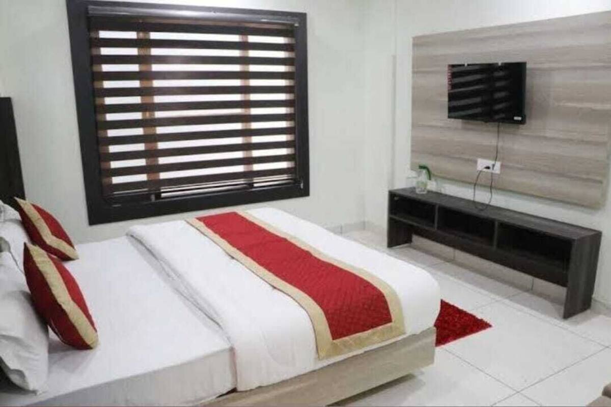 A hotel room with a bed, a TV mounted on the wall, and a window with blinds.