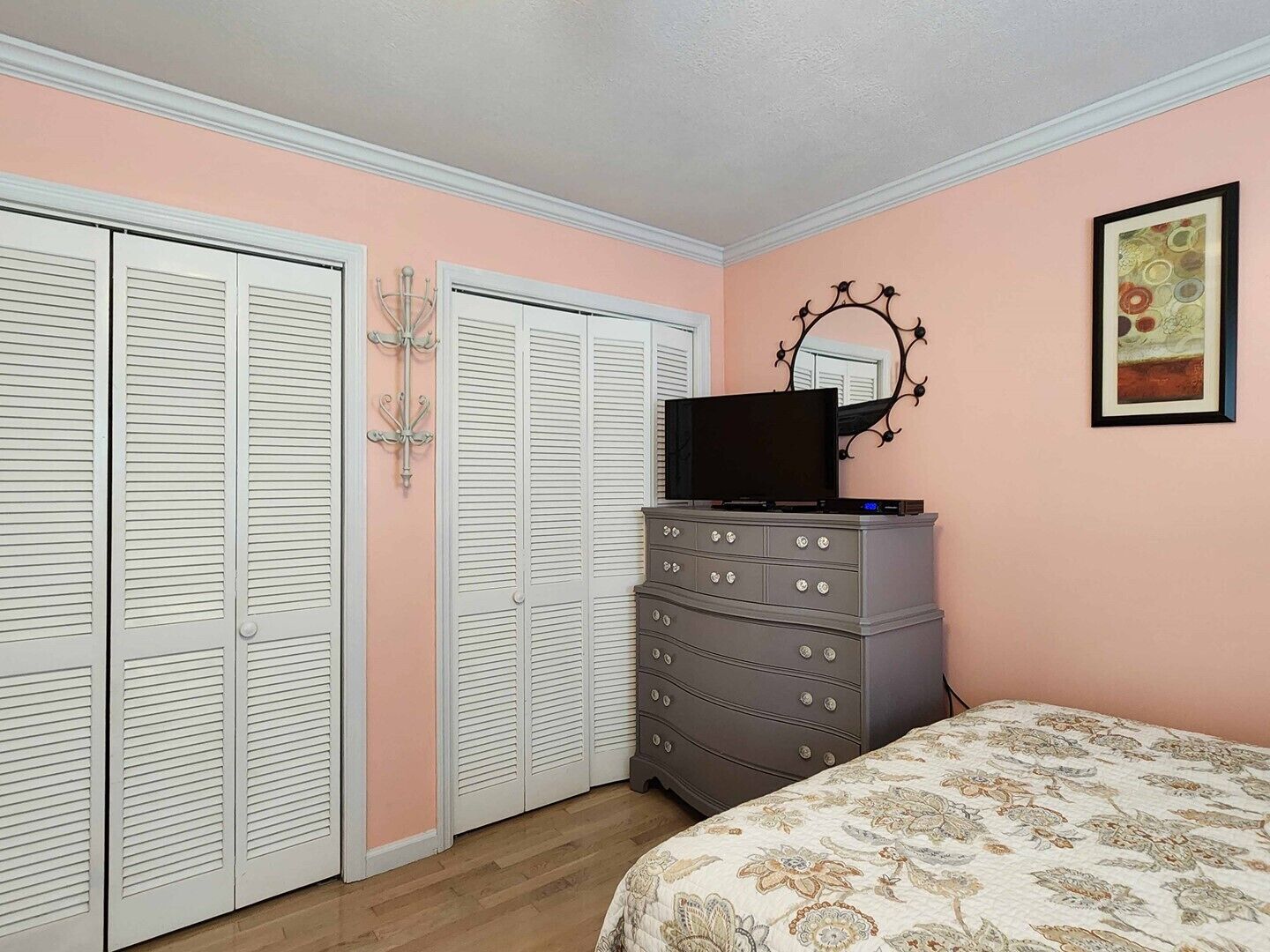 A bedroom with a bed, a dresser, a television on top, and a closet with louvered doors.