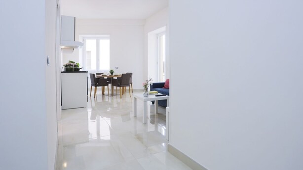 A modern kitchen with white cabinetry, a dining area with a table and chairs, and a living space with a sofa and a coffee table. - GuesHost - Positano Apartment in Salerno (Salerno)