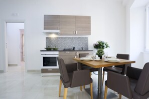 A modern kitchen with a dining area, featuring a wooden cabinet, a tiled backsplash, and a dining table with chairs. - GuesHost - Positano Apartment in Salerno (Salerno)