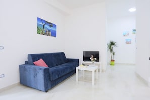 A living room with a blue sofa, a white coffee table, a flat-screen TV, and a potted plant. - GuesHost - Positano Apartment in Salerno (Salerno)