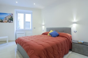 A bedroom with a bed, bedside table, and a window with blinds. - GuesHost - Positano Apartment in Salerno (Salerno)