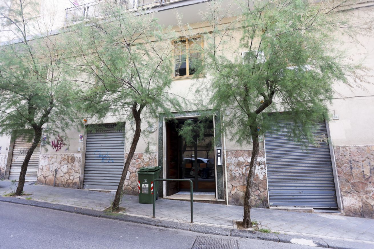 A building with a stone facade, a metal door, and a green trash bin.