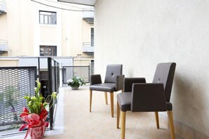 Ein Balkon mit drei Stühlen, einer Topfpflanze und einem Metallgitter.