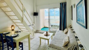 A living room with a staircase, a dining area, a sofa, and a view of the sea through a glass door. - Apartment with sea view - 4 guests (Fouras)