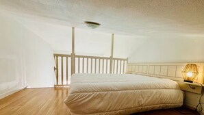 A bedroom with a wooden floor, a bed with a white mattress and headboard, and a bedside table with a lamp. - Apartment with sea view - 4 guests (Fouras)