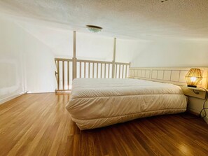 A bedroom with a wooden floor, a bed with a white mattress and headboard, and a bedside table with a lamp. - Apartment with sea view - 4 guests (Fouras)