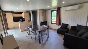A modern living space with a dining table, sofa, kitchen area, and large windows. - Comfort Chalet with AC & Parking / 2 Bedrooms (Marzan)