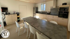 A modern kitchen with a large island, white chairs, and built-in appliances. - Family Home 700m from Beach, Spa, Pets Allowed (Saint-Hilaire-de-Riez)