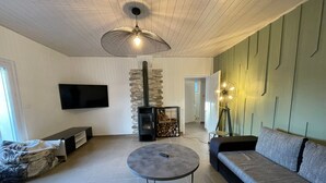 A modern living room with a fireplace, a round coffee table, a sofa, and a TV mounted on the wall. - Family Home 700m from Beach, Spa, Pets Allowed (Saint-Hilaire-de-Riez)