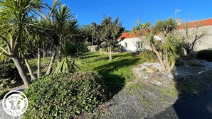 A residential property with a well-maintained lawn, palm trees, and a white building with a red roof. - Family Home 700m from Beach, Spa, Pets Allowed (Saint-Hilaire-de-Riez)
