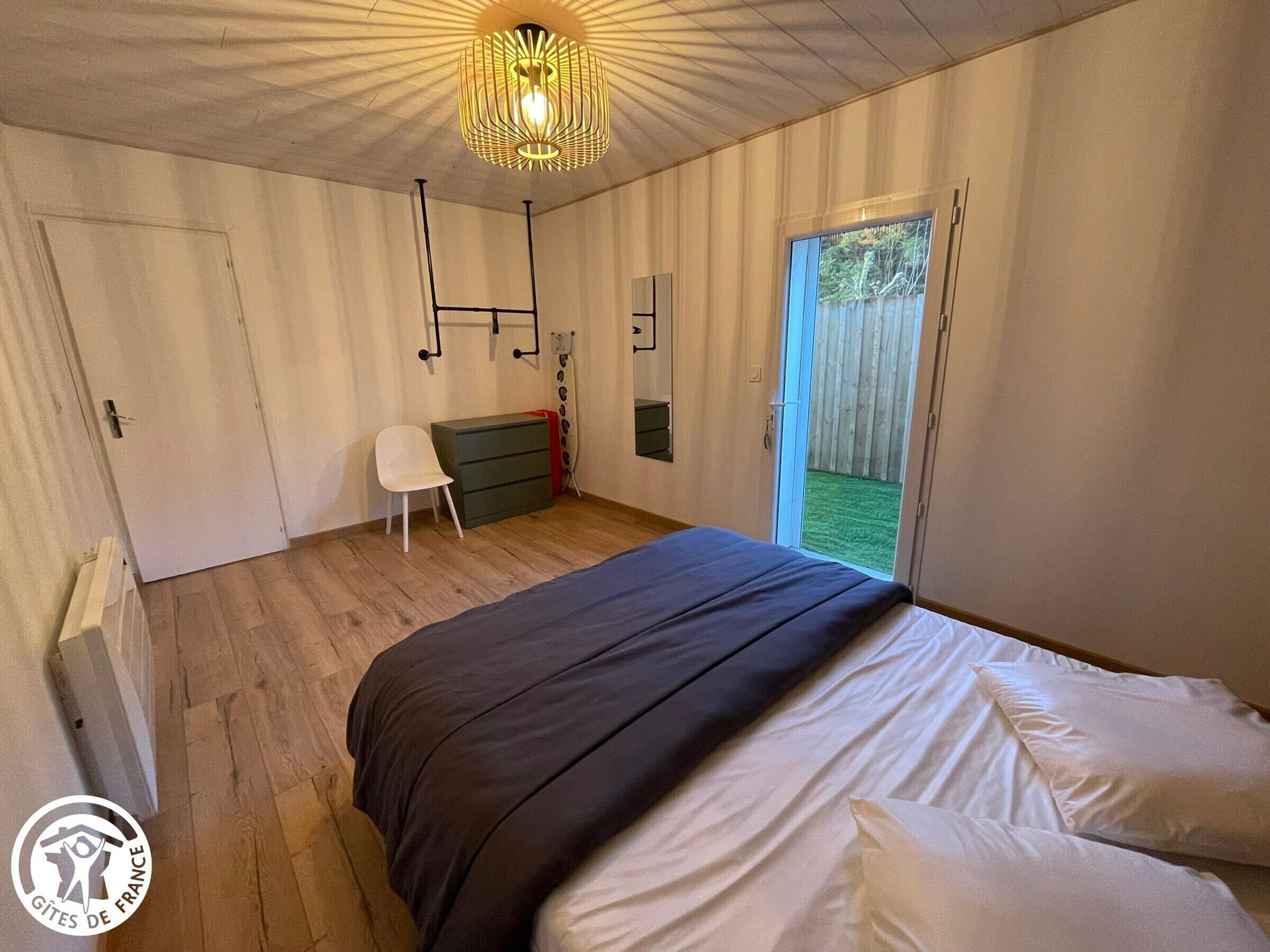 Une chambre à coucher avec un lit, une chaise, une commode et une grande fenêtre.