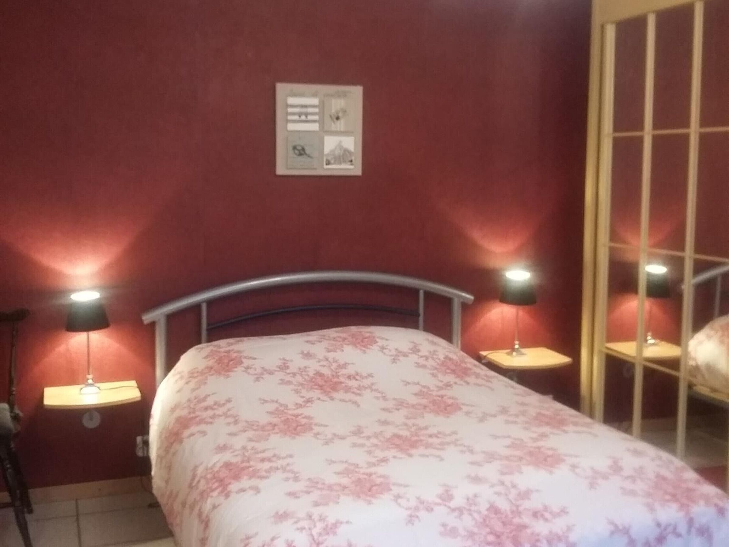 A bedroom with a bed, two bedside lamps, a wall-mounted clock, and a window with a view.