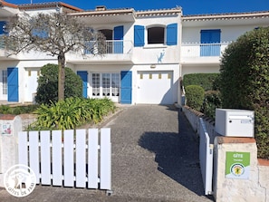 Un bâtiment à deux étages, doté d’une façade blanche, de volets bleus et d’une entrée fermée par un portail.