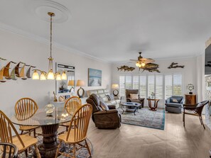 A spacious living room with a glass dining table, comfortable seating, and decorative elements like wall art and a ceiling fan. - 2 Bedroom Beach Manor condo on the 7th Floor at Tops’l Resort with Sandestin Resort Perks!! (Miramar Beach)