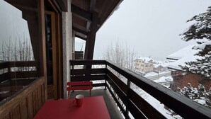 Un balcon avec une table rouge et deux chaises rouges, donnant sur un village enneigé.