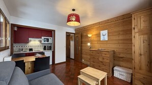 Un espace de vie compact comprenant un coin cuisine, un mur en bois, un canapé, une petite table et une lampe.