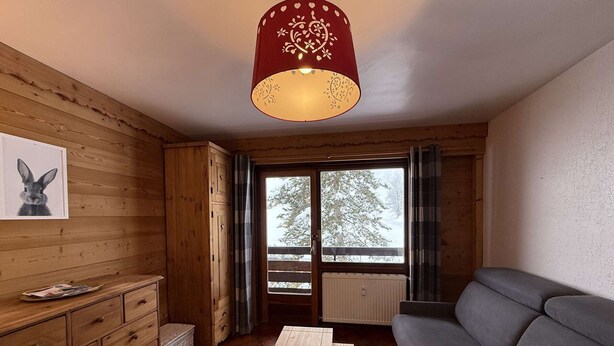 Une pièce chaleureuse avec des murs en bois, un canapé gris, une table en bois et une fenêtre donnant sur des arbres.