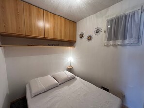 A bedroom with a bed, wooden cabinets, a nightstand, and decorative wall art. - Charming 2-room apartment by Lake Vonnes with terrace (Châtel)