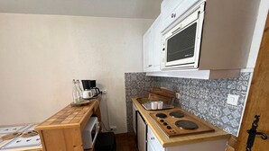 A compact kitchen with a stove, a coffee maker, and a microwave. - Charming 2-room apartment by Lake Vonnes with terrace (Châtel)