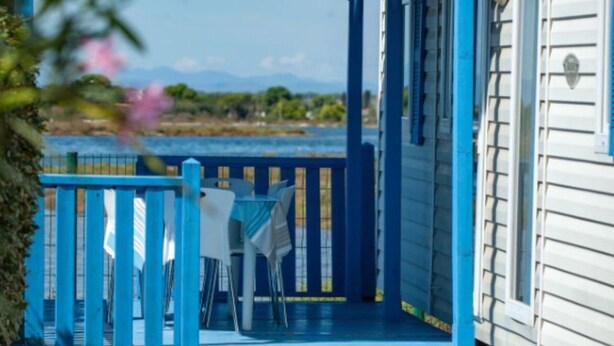 A covered outdoor area with a view of a body of water and mountains, featuring a blue railing and white chairs. - 3-bedroom mobile home with terrace in Marseillan (Marseillan)
