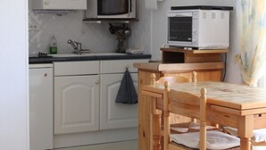 A kitchen with white cabinets, a microwave, a toaster, and a wooden table with chairs. - Apartment near sea with private parking, quick beach access (Fort-Mahon-Plage)