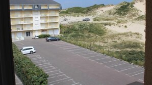 A multi-story hotel with a parking lot in front, adjacent to a sandy dune landscape. - Apartment near sea with private parking, quick beach access (Fort-Mahon-Plage)