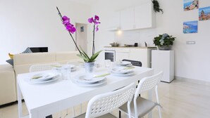 A modern dining area with white furniture, a white table set for four, and a kitchen in the background. - Bright apartment totally new both in terms of renovation and furnishings, accommodates up to 6 people and is located in a very central district: just 5 minutes walk from Corso Vittorio Emanuele, in an area fully served by shops including pharmacy, post o (Salerno)