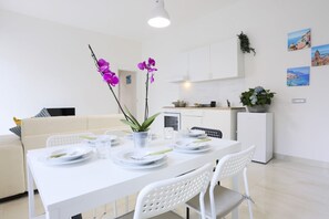 A modern dining area with white furniture, a white table set for four, and a kitchen in the background. - Bright apartment totally new both in terms of renovation and furnishings, accommodates up to 6 people and is located in a very central district: just 5 minutes walk from Corso Vittorio Emanuele, in an area fully served by shops including pharmacy, post o (Salerno)