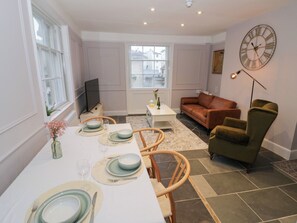 A dining area with a table set for four, a sofa, a green armchair, and a clock on the wall. - 12 Montpellier Arcade (Cheltenham)